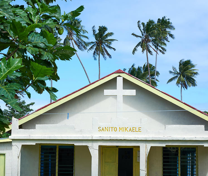 The roofline of a church against a backdrop of blue sky and palm trees