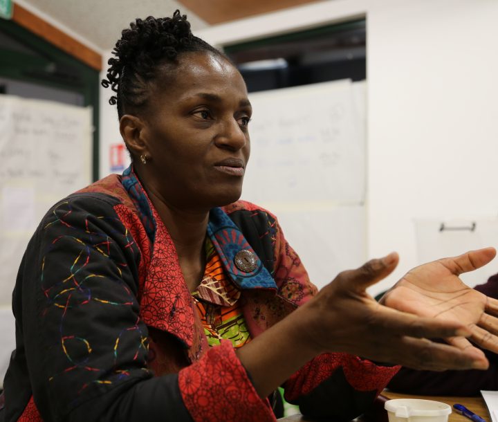 A woman talking in a meeting faces the camera, her palms facing upwards