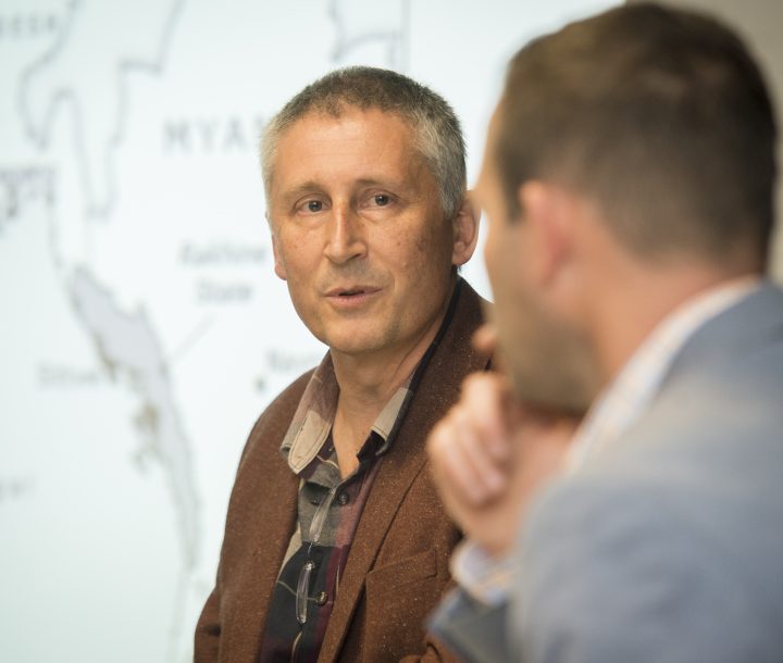 Two men in discussion, one facing the camera and the other lookng away.