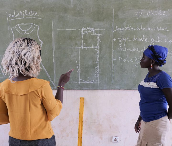 Two women stand facing a blackboard, looking at the chalk writing