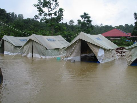 A row of tents with the UNOCHA logo printed ontop are surrounded by brown water.