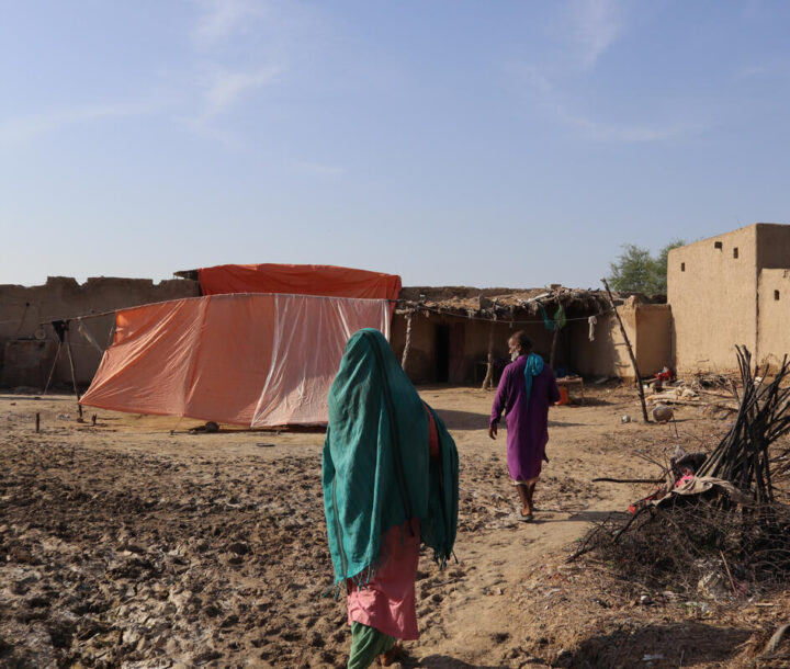 A woman wearing a green cloth walks away from the camera. There is a man and a plastic tent in the background