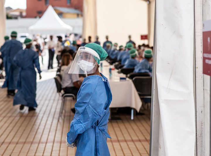 A male wearing a surgical gown and mask stands in front of a long table.