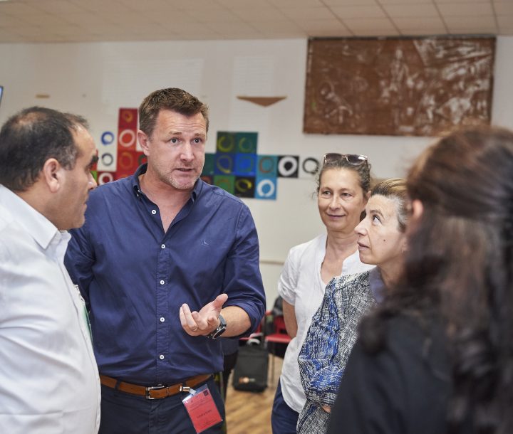 A group of five people face each other. A man in a blue shirt is talking while the others are listening.