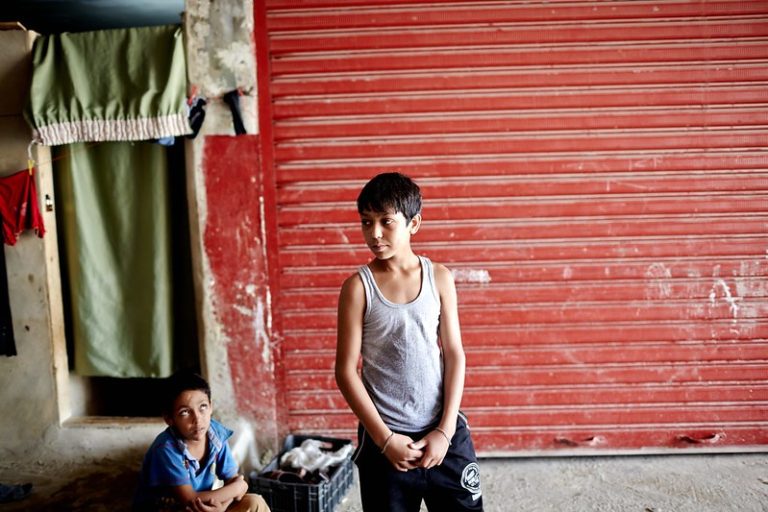A small boy in a grey singlet stands in front of a red wall.
