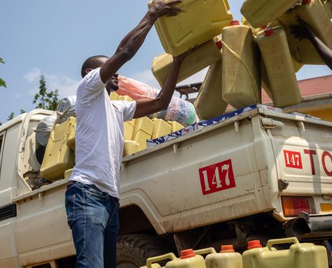 A man stands to the side of a utility vehicle and is holding a yellow container.